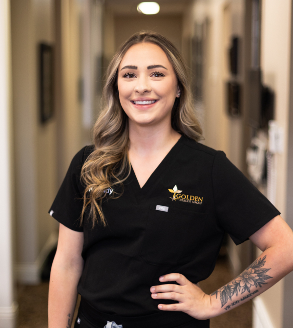 Kassidy, the massage therapist, is dressed in a black medical uniform and smiling.